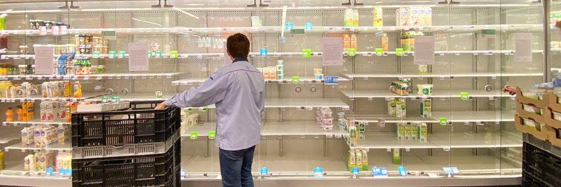 Man standing in front of empty shelves in supermarket trying to restock product
